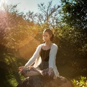 Home 2 Woman sitting on a rock and meditating surrounded by trees